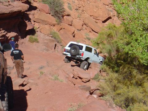 1993 Ford Bronco - A white 1993 Ford Bronco navigates a steep, rocky incline in a desert landscape.