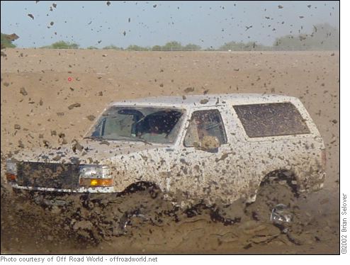 White SUV, heavily mud-caked, driving through a mud pit