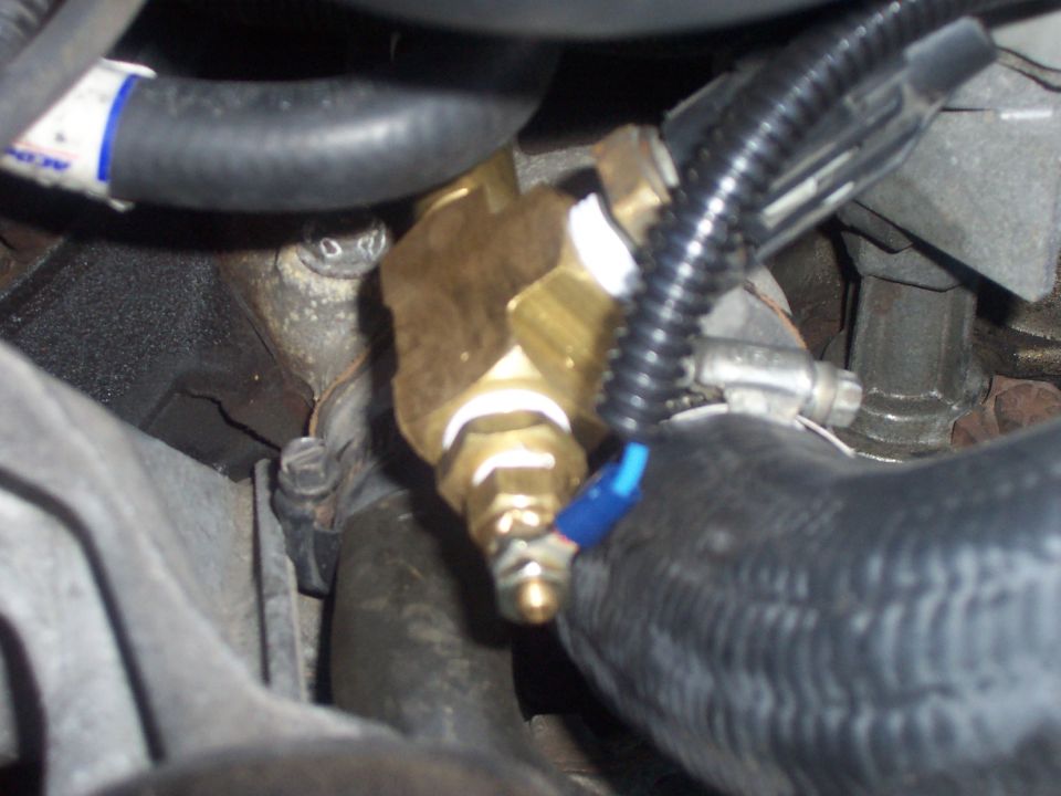 Brass tee fitting and sender threaded into an engine block among heater hoses