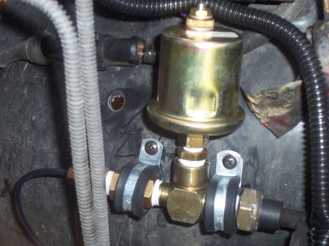 1994 Ford Bronco - This is a close-up view of an oil pressure gauge sender unit, showing its brass fittings and gold-colored housing.