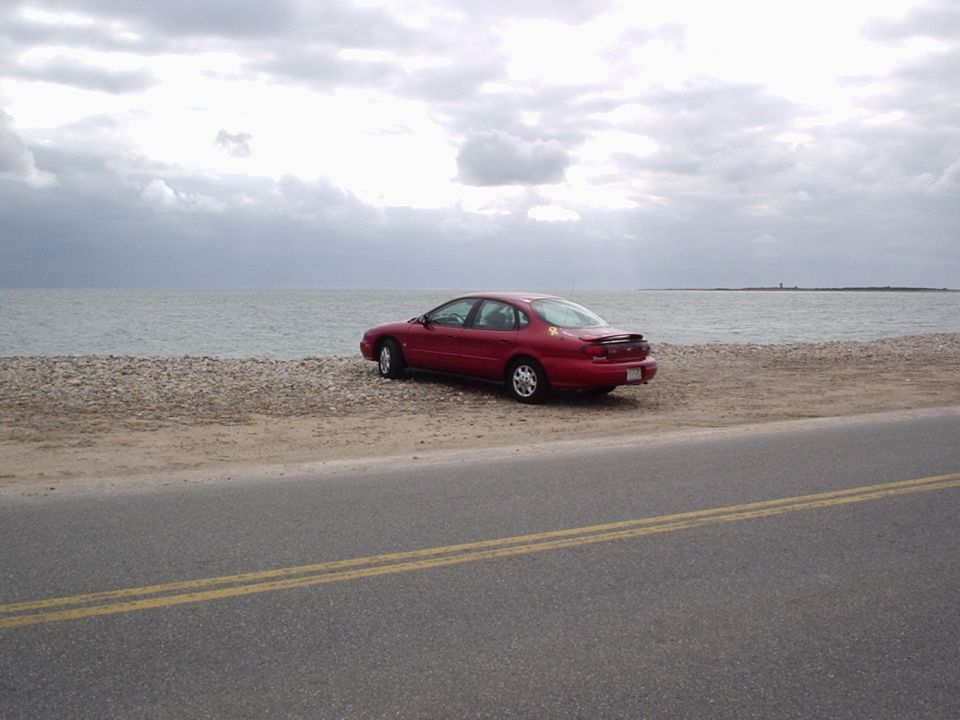 Red 1998 Ford Taurus parked on a beach with the ocean in the background