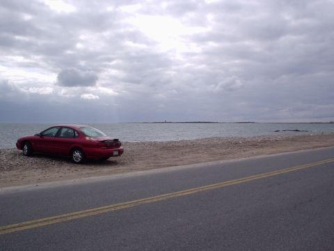 1998 Ford Taurus - Red 1998 Ford Taurus parked on a beach with the ocean in the background.