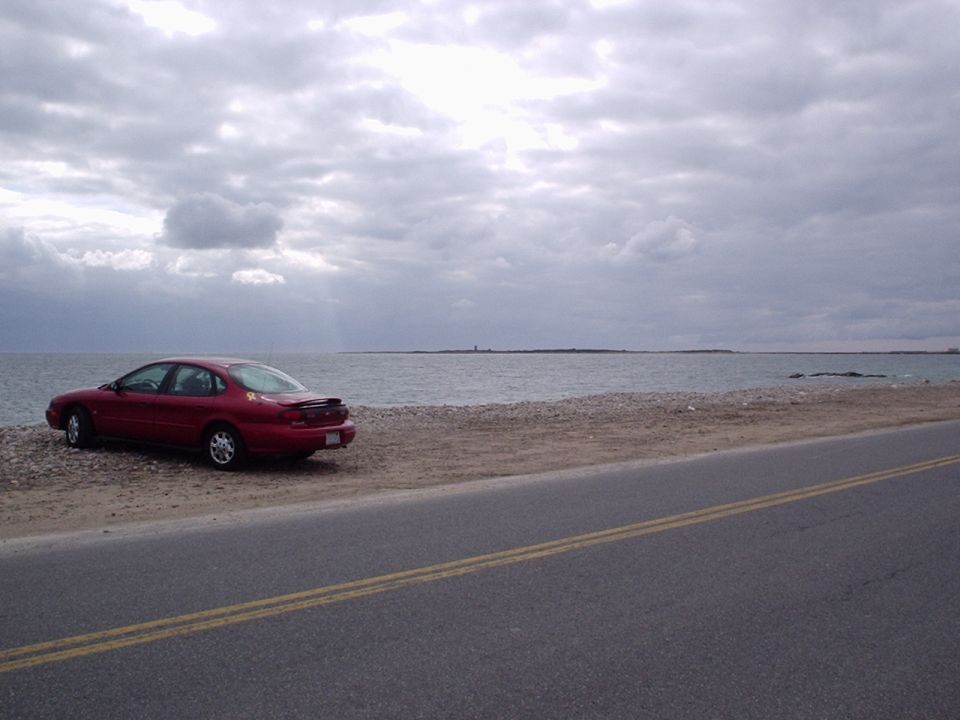 1998 Ford Taurus parked on beach by the water under cloudy sky
