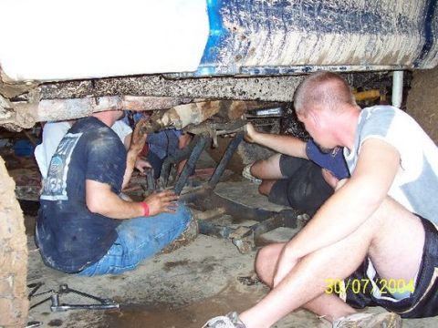 1979 Ford F-150 - Men work on the underside of a truck chassis, with the blue body of the vehicle overhead.