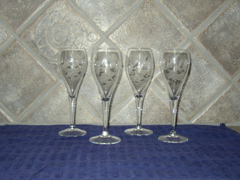 Four etched champagne flutes on a blue cloth in front of a tiled wall