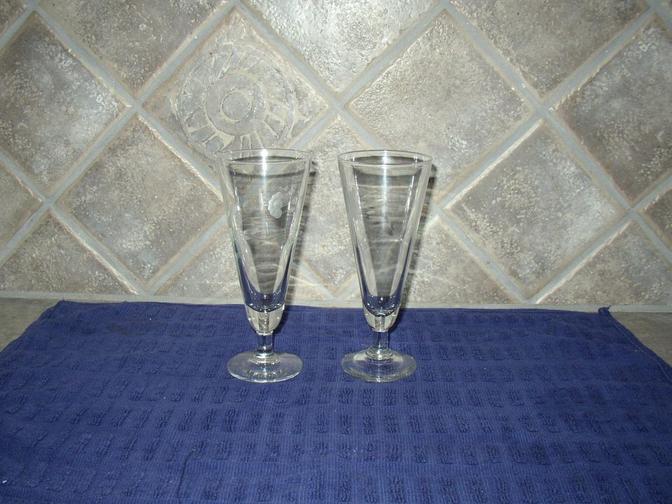 Two clear stemmed glasses with etched patterns, placed on a blue textured cloth against a tiled background
