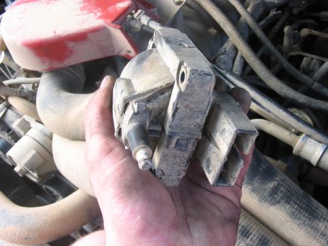 1988 Ford Bronco - A hand holds a dusty engine part, surrounded by hoses and wiring, suggesting a repair or upgrade.