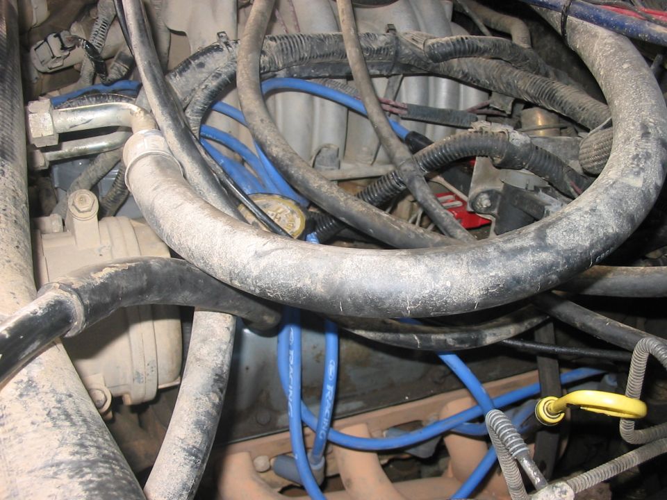 Engine bay with blue spark plug wires and black hoses, covered in dust
