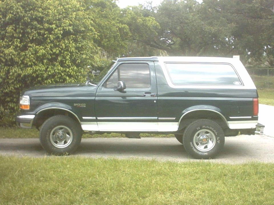 Dark green Ford Bronco with white top, driver-side profile on a driveway