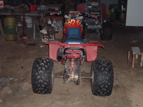 1995 Mercury Grand Marquis - This red ATV has flame decals and is parked in a garage next to another vehicle.