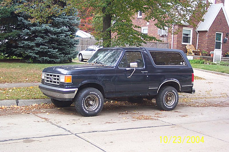 Dark blue 1987 Ford Bronco parked on a street, side view. Some rust visible