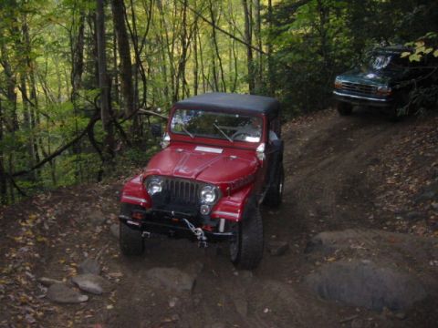 1996 Ford Bronco - Two off-road vehicles navigate a challenging dirt path through a forest.