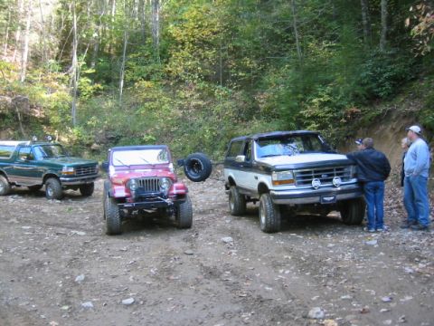 1996 Ford Bronco - Three SUVs parked on a dirt road in a wooded area, with people standing near one of the Broncos.