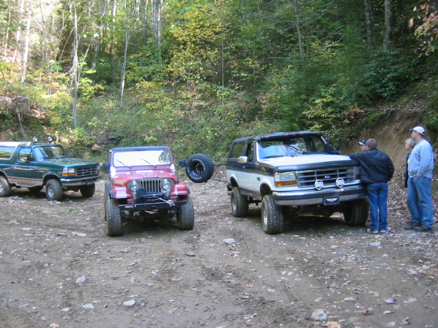 Green Ford Bronco, red Jeep, and white/black Ford Bronco on a dirt road