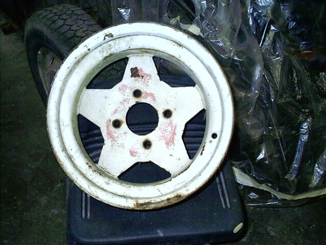 Rusty white five-spoke four-lug wheel leaning on a black step stool in a garage