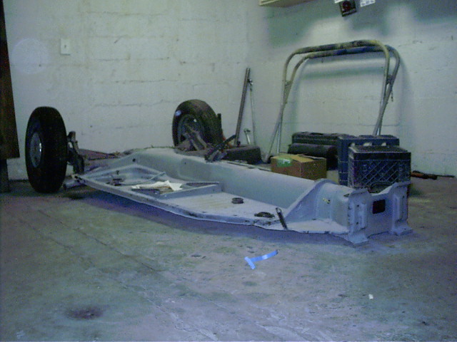 Bare gray VW Beetle floor pan chassis with front wheels in a garage during restoration