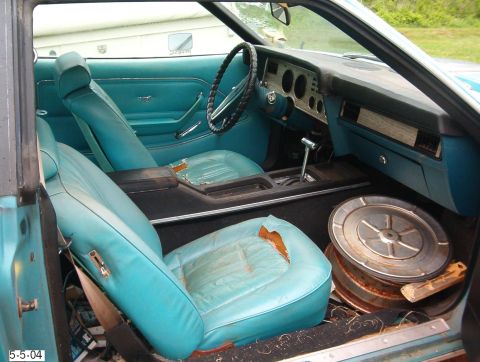 1977 Ford Mustang II - The interior of a 1977 Ford Mustang II shows worn blue upholstery and a dashboard with woodgrain accents.