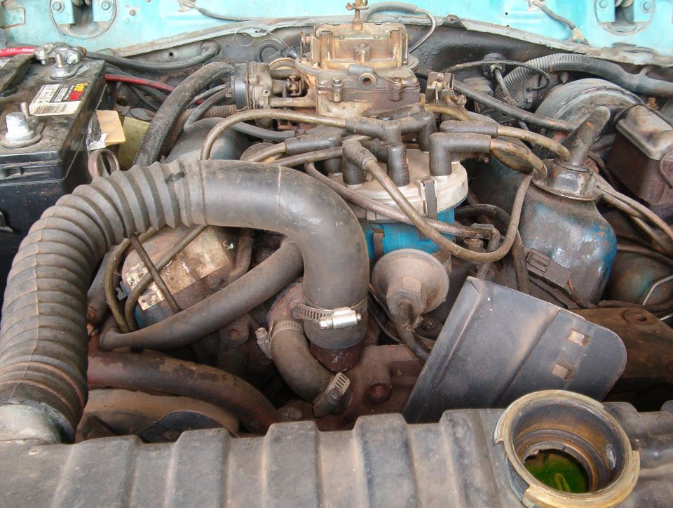 engine bay with carburetor, distributor, battery, and hoses