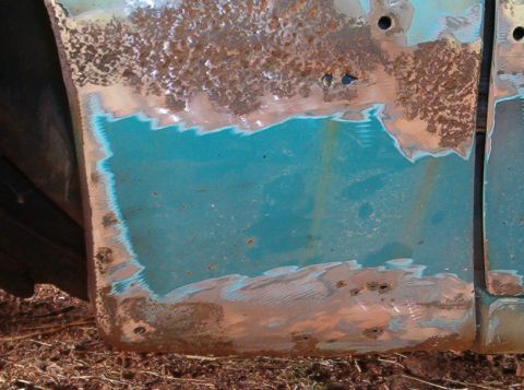 1977 Ford Mustang II - This close-up shows significant rust and primer on a car door, indicating a restoration project in progress.