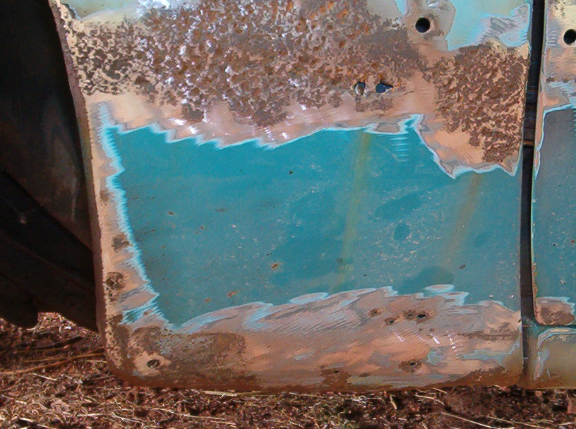 Rusted teal car door with primer and metal showing, undergoing restoration