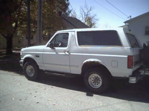 1993 Ford Bronco - This white Ford Bronco is parked on a residential street, showing its side profile with some visible rust.