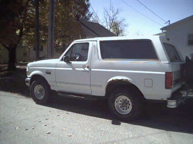 White Ford Bronco parked on a street, side view. Some rust visible on rear wheel well