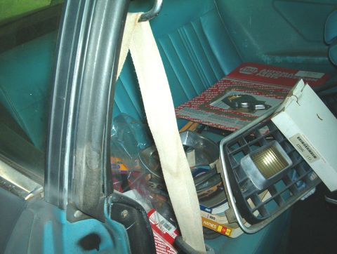 1977 Ford Mustang II - A collection of auto parts is stored inside a car with turquoise upholstery.
