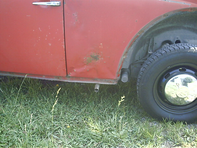 Lower rear quarter of red car with black steel wheel and chrome hubcap, parked on grass