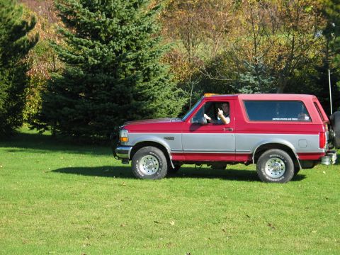 1995 Ford Bronco - A two-door Ford Bronco with a red and silver two-tone paint scheme sits on a lawn with trees in the background.