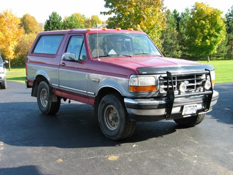 1995 Ford Bronco - This two-tone Ford Bronco is parked on a driveway with trees in the background.