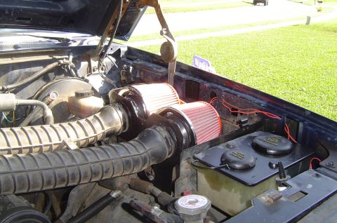 1993 Ford Bronco - Close-up of an engine bay with aftermarket air filters and intake system. The vehicle's dark blue exterior is visible along the fender.