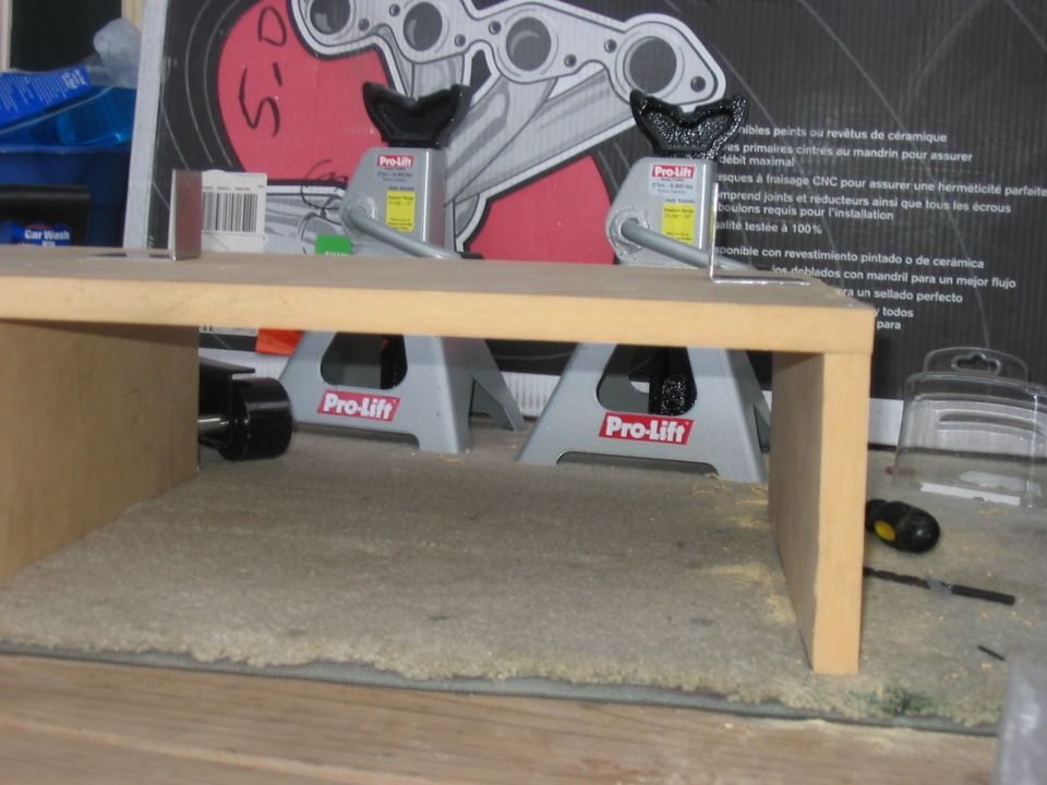 Two Pro-Lift jack stands supporting a wooden platform. A black tire is visible on the left