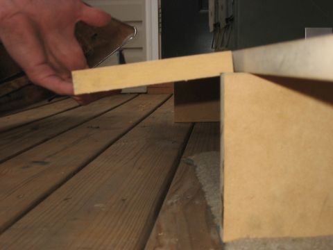1988 Ford Bronco - A hand holds a piece of wood over a deck or floor made of wooden planks.