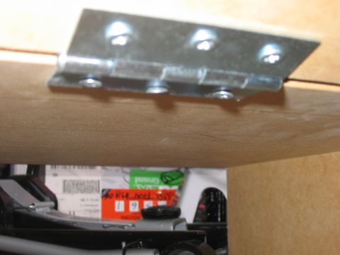 1988 Ford Bronco - A close-up view of a metal hinge mounted on a wooden panel, with items stored underneath.
