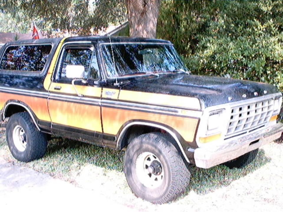 Ford Bronco with black top and orange/yellow side stripe. Front grille visible