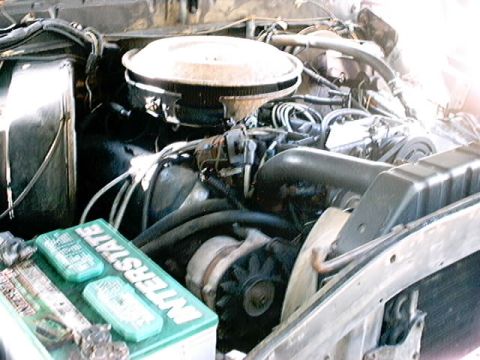 1979 Ford Bronco - The engine bay of a vehicle shows an Interstate battery and various engine components.