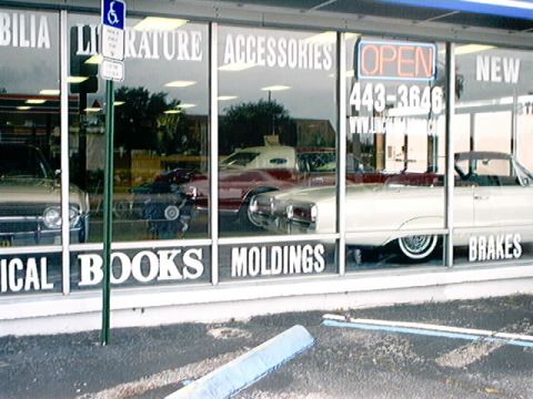 1979 Ford Bronco - Multiple vehicles are reflected in the large windows of a store, with text visible on the glass.