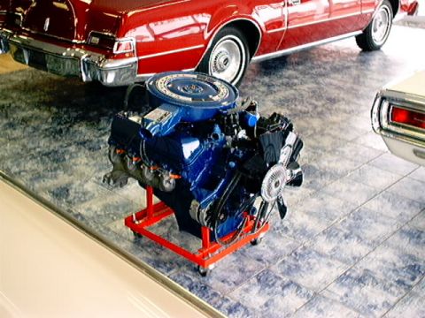 1979 Ford Bronco - A blue engine sits on a red stand in front of a red car.