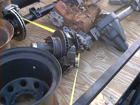 1979 Ford Bronco - Vehicle axles, brake components, and a rusty engine block are displayed on a wooden surface.