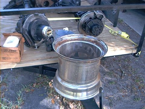 1979 Ford Bronco - Various vehicle parts, including a wheel and brake components, are loaded onto a trailer for transport.