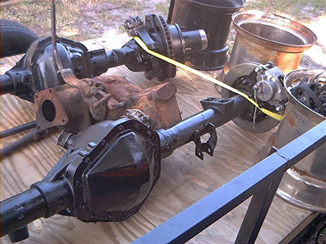 Two black vehicle axles with brake components and differential covers on a wooden surface