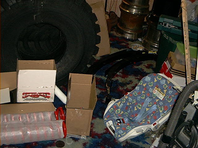 Baby car seat with a blue, patterned cover sits next to a large tire and cardboard boxes
