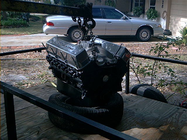 Engine with chrome valve covers that say Ford Racing, suspended by a crane
