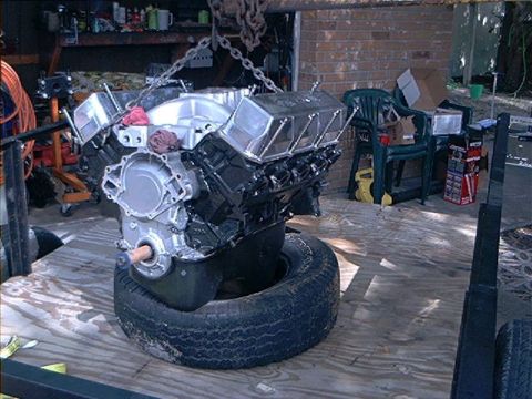 1979 Ford Bronco - Engine assembly is hoisted by chains, resting on a tire, ready for installation or repair.