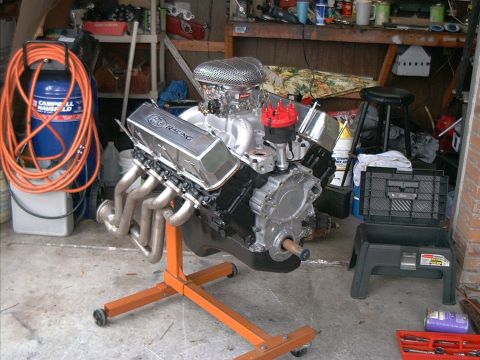 1979 Ford Bronco - A V8 engine with chrome valve covers and headers sits on an engine stand in a cluttered garage.