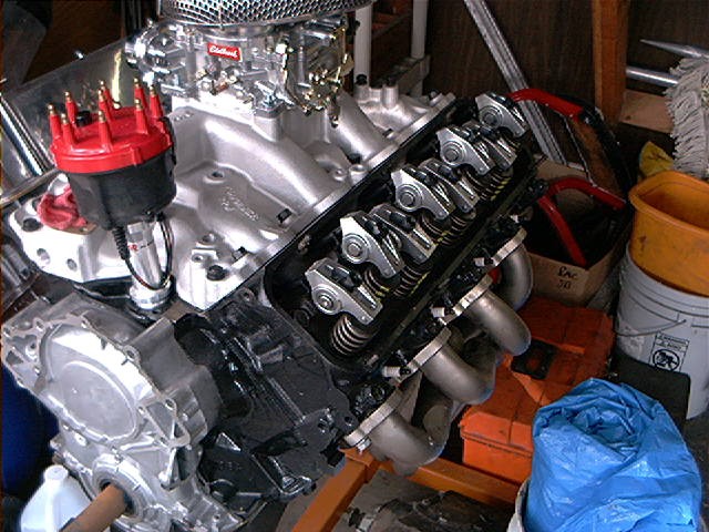 Engine block with valve covers removed, showing rocker arms and springs. Chrome air cleaner and red distributor cap visible