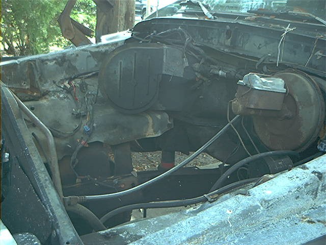 Engine bay with master cylinder and brake booster visible, showing significant damage and rust