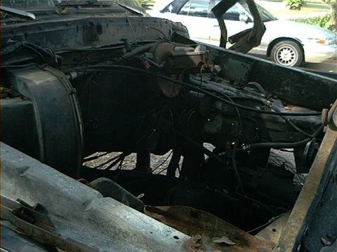 1979 Ford Bronco - The engine bay of a vehicle is shown, with another car visible in the background.