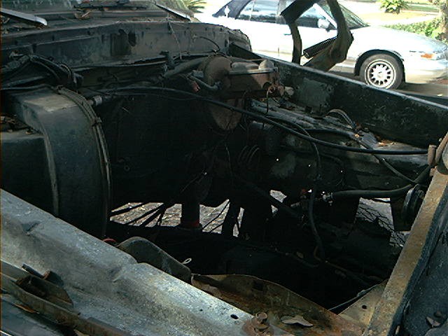 engine bay of a dark colored vehicle, with a white car in the background