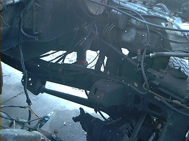 close-up of vehicle frame, suspension, and engine components, appears to be disassembled or damaged